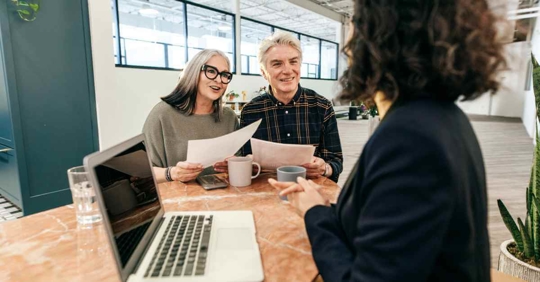 A man and woman sitting across from an attorney. The man and woman have papers in their hands and smiles on their faces.