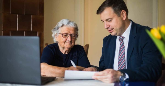 A man sitting next to an older woman helping her fill out paperwork