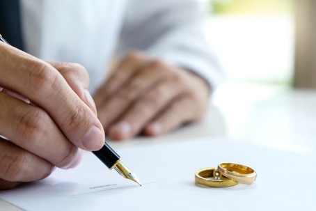 man signing prenup with wedding rings